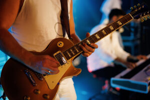 A close-up shot of a guitarist playing their guitar live on stage.